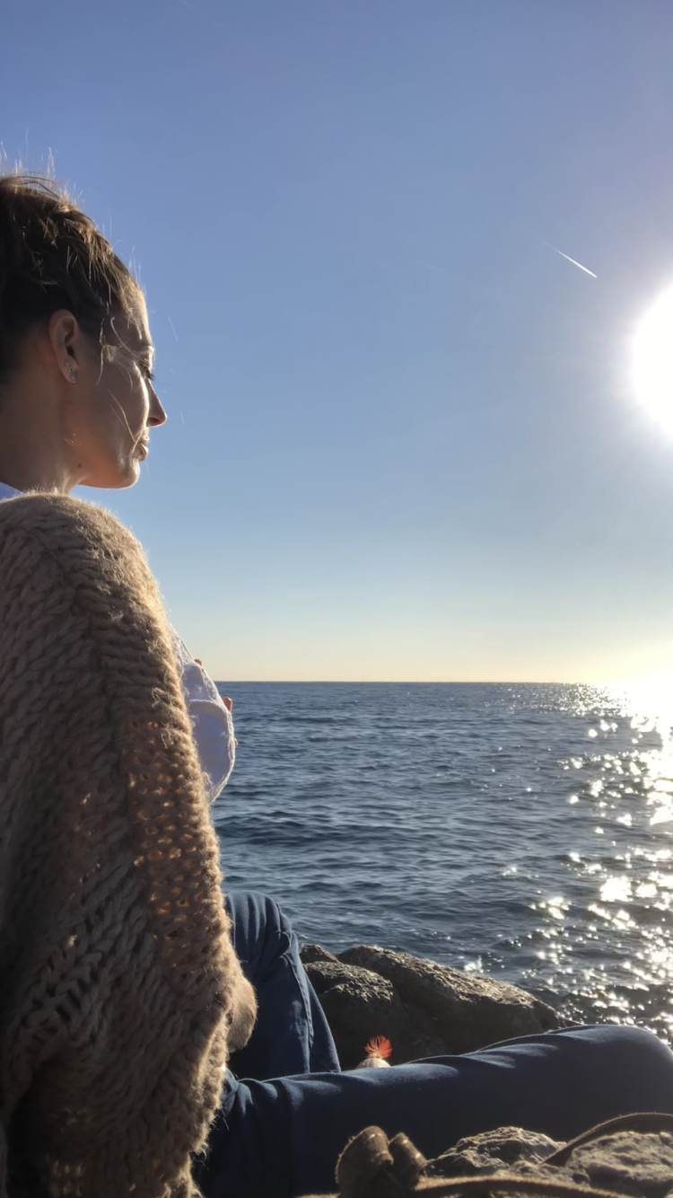 Chloé assis sur un rocher au bord de mer devant le soleil